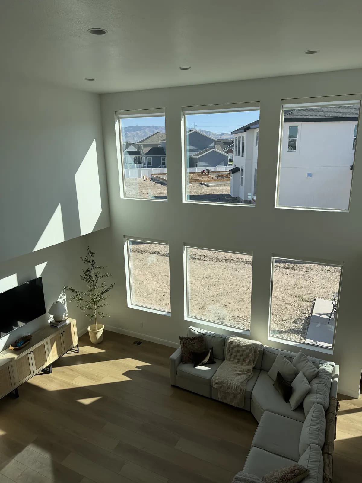 Two-story great room with a wall of tall windows fitted with motorized roller shades, sectional sofa in the foreground